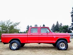 a red pick up truck parked on top of a dry grass field next to trees