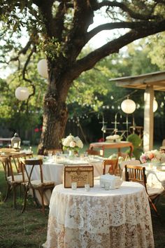 the table is set for an outdoor wedding reception under a large tree with hanging lanterns