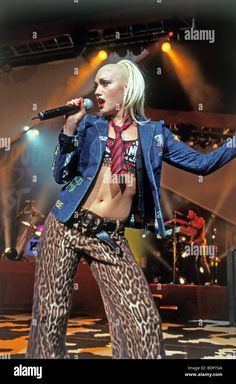 the blond haired woman in leopard print pants singing into a microphone on stage at a concert - stock image