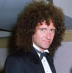 a man with curly hair wearing a tuxedo and bow tie in a room