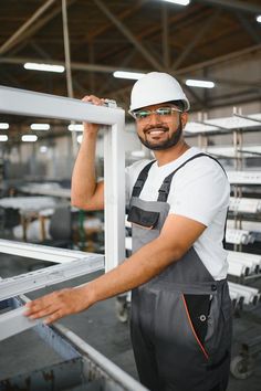 Happy bearded Indian male factory worker in special uniform and white hard hat holding aluminum frame at production of royalty free stock photos