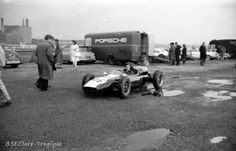 an old photo of a man in a race car on the ground next to other cars