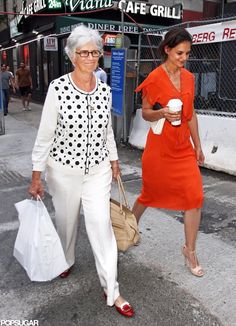 two women are walking down the street with bags and coffee in hand, one is carrying a paper bag