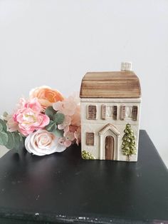there is a small house next to some flowers on the black table with white walls