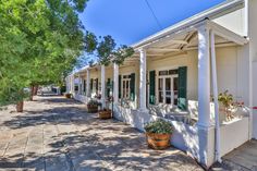 a row of white houses with green shutters on the front and side windows, lined with potted plants