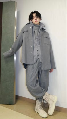 a man standing in front of a wall with his hands on his hips wearing grey pants and jacket