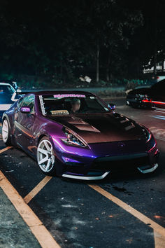 a purple sports car parked in a parking lot next to other cars on the street