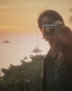 a man taking a selfie in front of the ocean with boats on the water