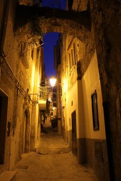 an alley way at night with lights on and stone buildings lining both sides, in the middle of town