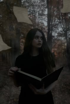 a woman standing in the woods holding a book