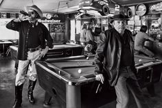two men in cowboy hats standing next to a pool table with cars on the ceiling