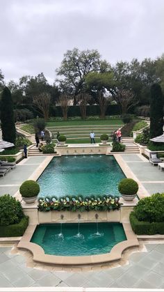 an outdoor pool with water features surrounded by trees and lawn furniture, as well as people walking on the other side