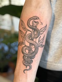 a tattoo on the arm of a man that has a snake and leaves on it