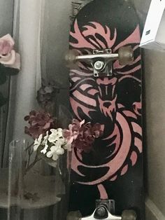 a skateboard with pink and black designs on it sitting next to a flower vase