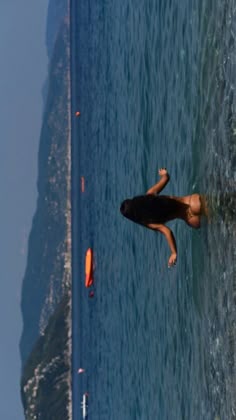 a woman is swimming in the ocean with an orange surfboard on her back and one hand up above her head