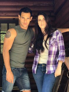 a man and woman standing next to each other in front of a wooden structure with windows