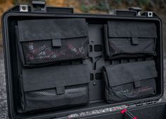 an open black case with four compartments on the inside and one in the outside, sitting on gravel
