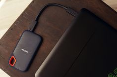 an external hard drive next to a laptop on a wooden table with a red cord