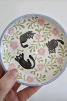 a hand holding a bowl with black cats on it and pink flowers around the bottom