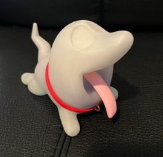 a white plastic dog with its tongue out on a black leather surface and it's mouth open