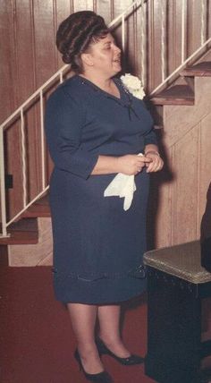 an old photo of a woman standing in front of a stair case holding a flower