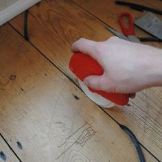 a person holding a red and white object on top of a wooden floor next to pliers