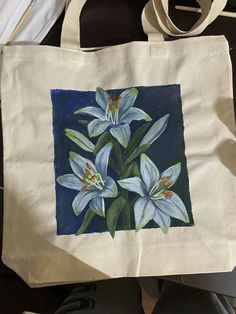 a painting of white lilies on a canvas tote bag, with shoes nearby