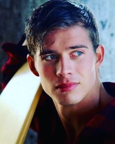 a close up of a person holding a surfboard in his hand and looking at the camera