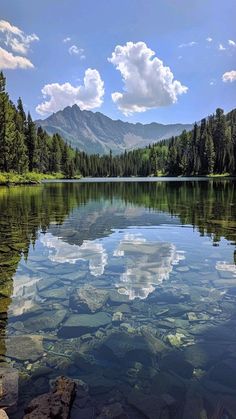 a lake surrounded by trees and mountains under a blue sky with puffy white clouds