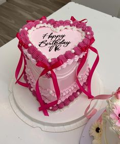 a heart shaped birthday cake with pink ribbon and flowers on the table next to it