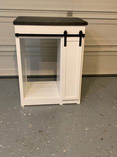 a small white cabinet with black top and bottom shelf on the floor next to a garage door