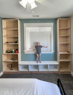 a young boy standing on a window sill in front of a bedroom with built - in bookshelves