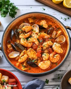 a pan filled with shrimp and clams in tomato sauce on top of a wooden table