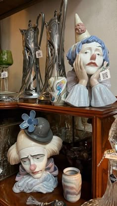 two ceramic clowns sitting on top of a wooden shelf next to cups and spoons