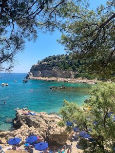 the beach is crowded with people and blue umbrellas in the water, while boats are out on the water