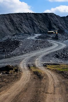 a truck driving down a dirt road next to a large pile of rocks and gravel
