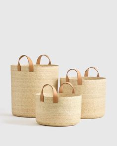 three baskets with handles are lined up against a white background, one is empty and the other has brown leather handles