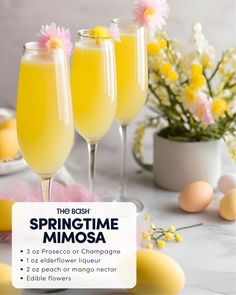 three glasses filled with yellow liquid sitting on top of a table next to eggs and flowers