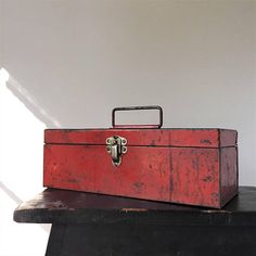 an old red metal box sitting on top of a black wooden table next to a white wall
