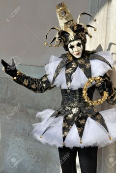 a woman wearing a costume with gold and white decorations on her face, standing in front of a wall