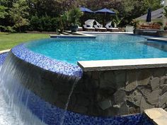 an outdoor swimming pool with waterfall and lounge chairs in the backround, surrounded by lush greenery