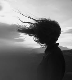 a woman with her hair blowing in the wind on top of a mountain at sunset