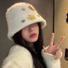 a woman wearing a white hat making the peace sign with her hand while standing in front of a mirror