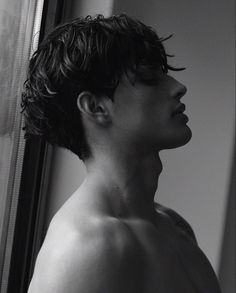 black and white photograph of a shirtless man looking out the window with his eyes closed