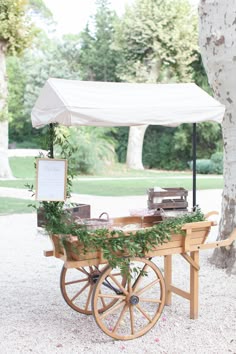 an old wooden cart with plants on it under a white tent in the middle of a park