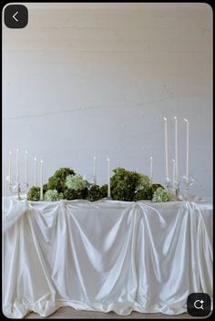 the table is covered with white cloth and lit candles are on top of each other