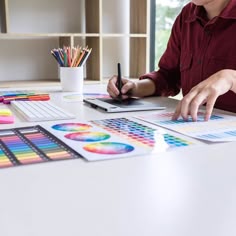a person sitting at a table with some colored pencils and papers on it,