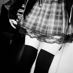 black and white photograph of woman in plaid skirt with knee high socks on her feet
