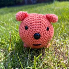 a small crocheted teddy bear sitting in the grass with it's eyes open