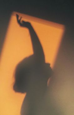 the shadow of a person's arm and hand on a yellow wall with light coming through it